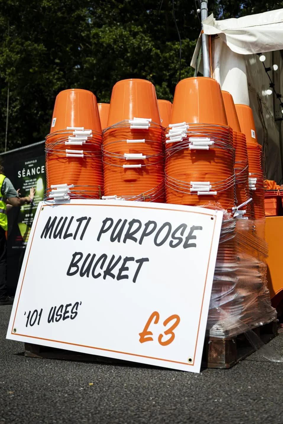 Stacks of orange multi purpose buckets beside a sign reading Multi Purpose Bucket, '101 uses'.