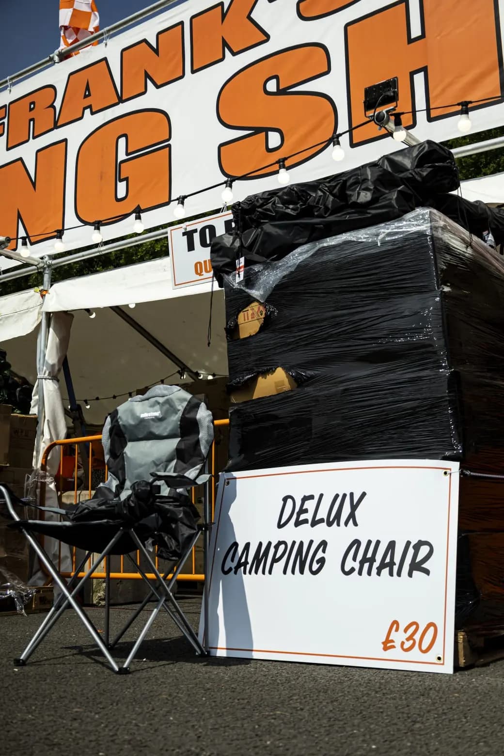 A folding camping chair set up beside its price sign, under the Fat Frank's Camping Shop banner.